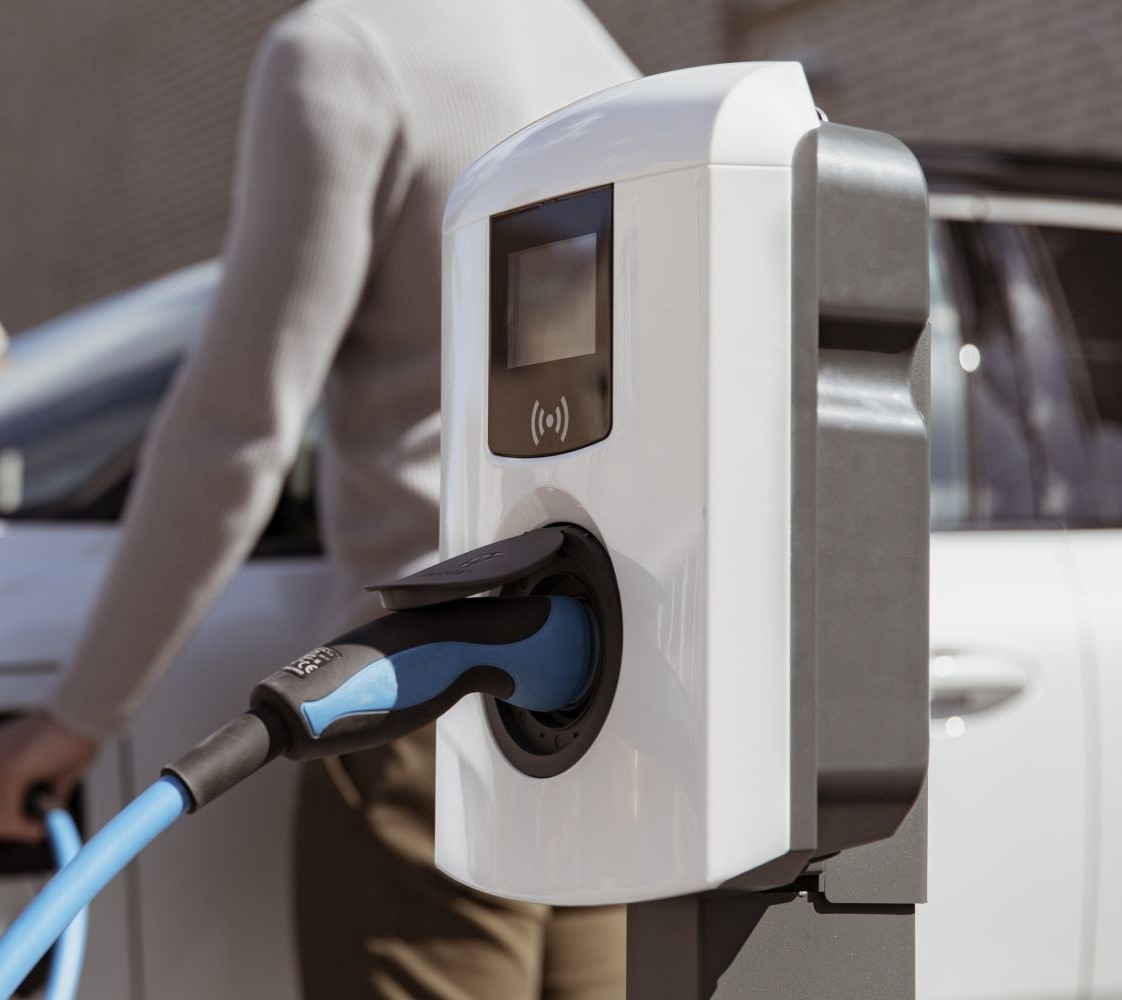 image of a EV charging point with a person standing next to it by a white car